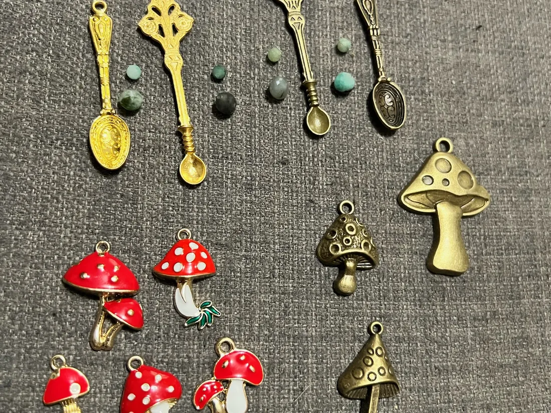 Colourful mushroom, key, gemstone, and metal charms arranged on grey fabric.