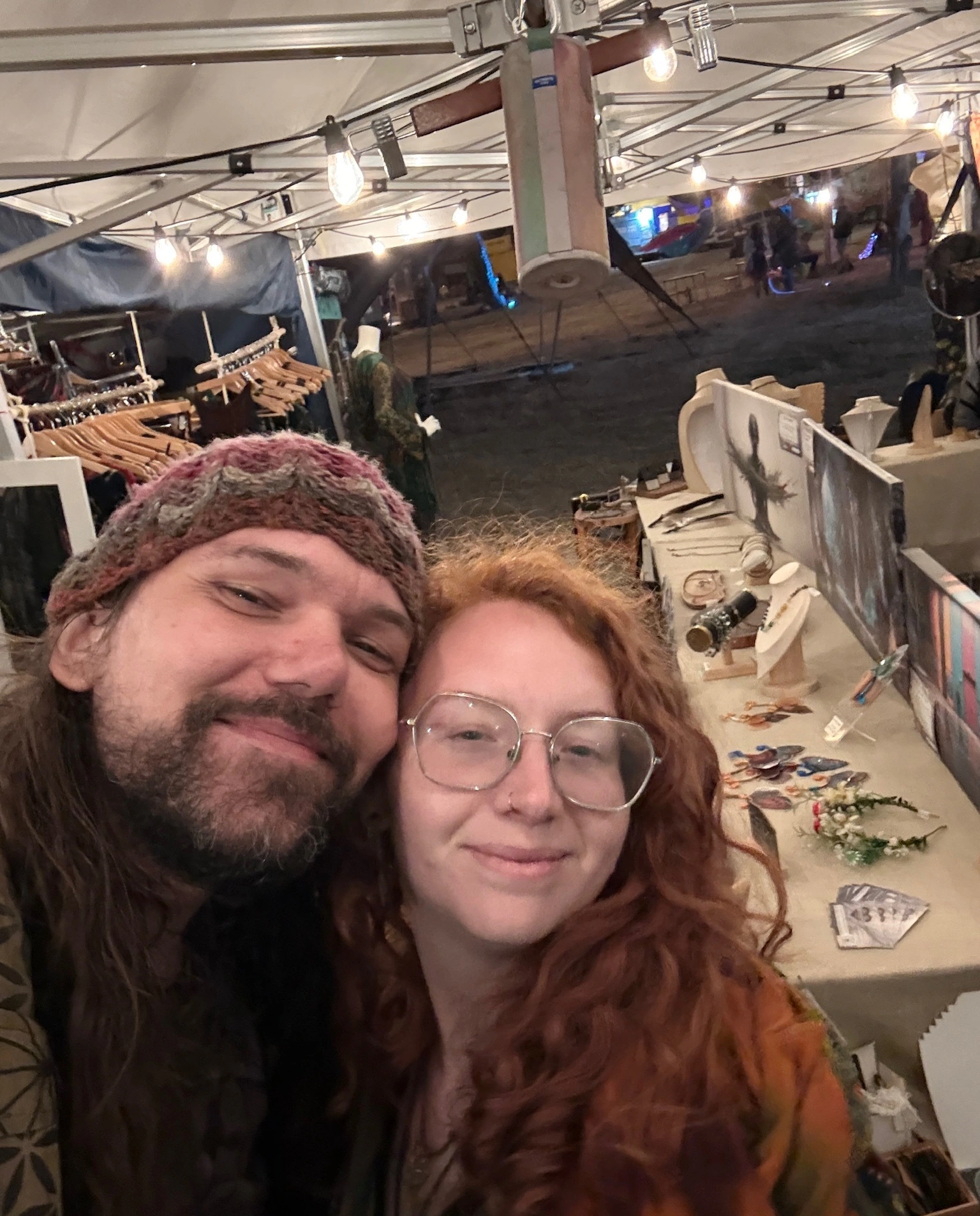 Michael and Charlie smiling together at their jewellery stall under warm market lights.